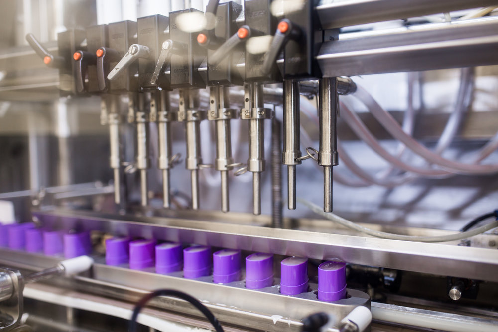 Close-up view of containers being filled with product in a packaging production line.