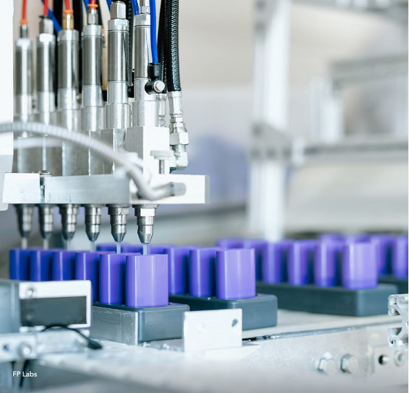 Automated machinery filling purple containers on a production line.