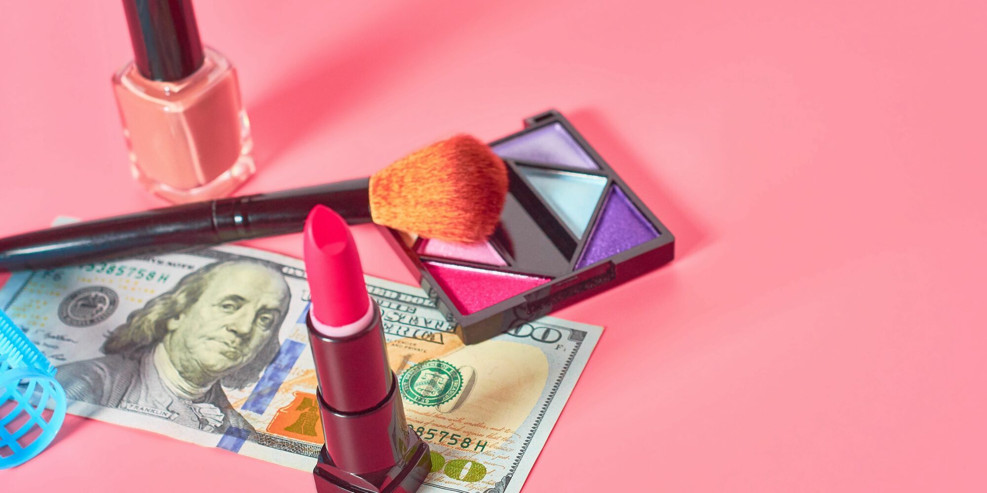 Various cosmetics accessories and banknote of 100 dollars on pink background. Concept of cost of beauty